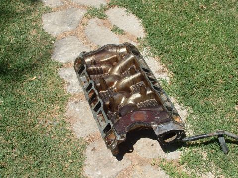 1990 Ford Bronco - A used engine intake manifold lies on the ground, showing signs of wear and grime.