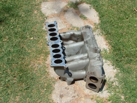 1990 Ford Bronco - This is an intake manifold, a component of an internal combustion engine, shown outdoors on a paved area.