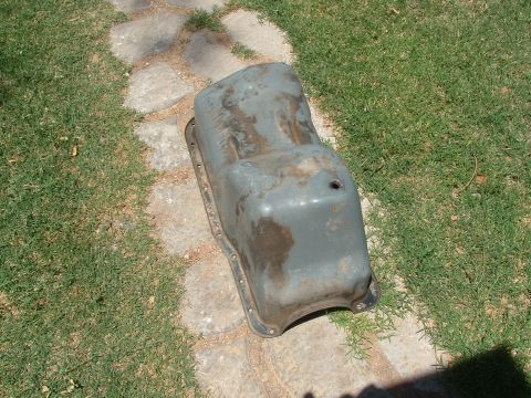 1990 Ford Bronco - A used oil pan sits on a path, showing signs of wear and rust.