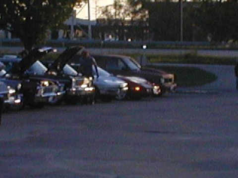 1998 Ford Taurus - Cars parked in a lot during twilight, with some headlights illuminated.