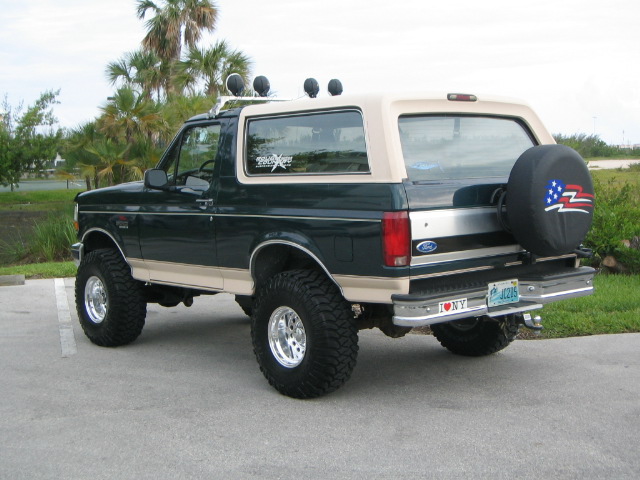 Lifted green and tan Ford Bronco, rear view, US-flag spare cover and roof lights