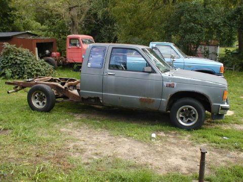 1998 Ford Taurus - A gray pickup truck chassis sits in a grassy yard with other vehicles in the background.