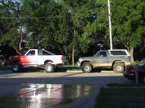 1988 Ford F-150 - Two lifted trucks, a Ford Bronco and a Ford pickup, are parked on a residential street.