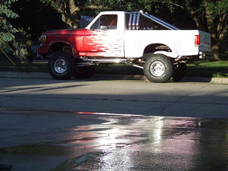 Lifted pickup truck, red front half with white flame graphics, white rear half, chrome roll bar with pipes