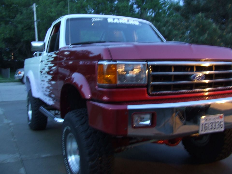 Red and white Ford F-150 truck, lifted with large tires. Custom graphic on the side. License plate reads 16-3336