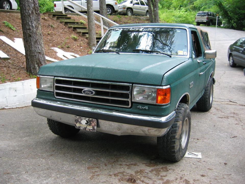 Green 1990 Ford Bronco with chrome bumper and 4x4 decal, parked on asphalt