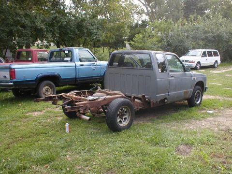 1998 Ford Taurus - A gray pickup truck chassis sits in a grassy area next to a blue pickup truck and a white van.