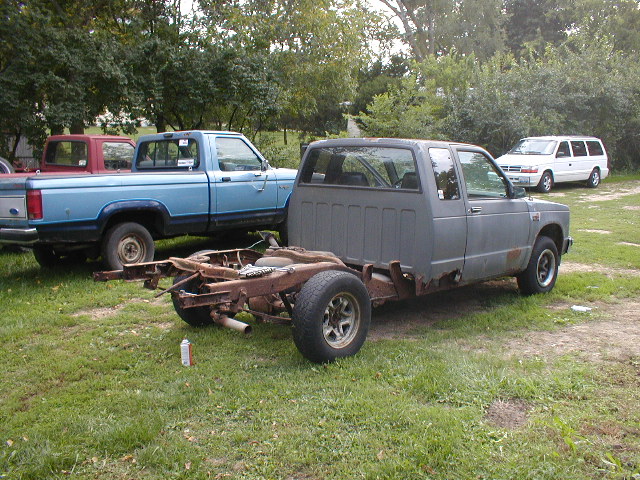 Gray pickup truck chassis with rusted frame, missing body panels, and one visible tire
