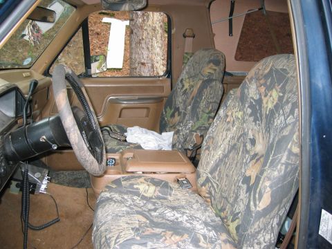 1990 Ford Bronco - The interior of the truck features camouflage seat covers and a CB radio, with trees visible through the windows.