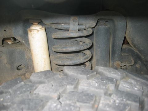 1990 Ford Bronco - Close-up view of the front suspension system, including a coil spring and shock absorber, with a tire visible in the foreground.