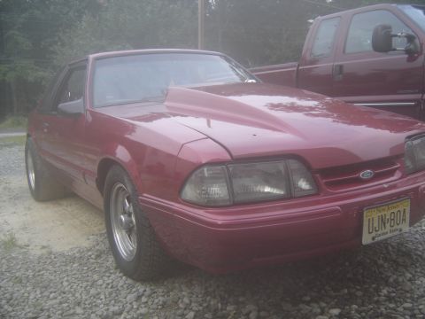 1988 Ford Bronco - A red coupe with an aftermarket hood is parked next to a maroon pickup truck.
