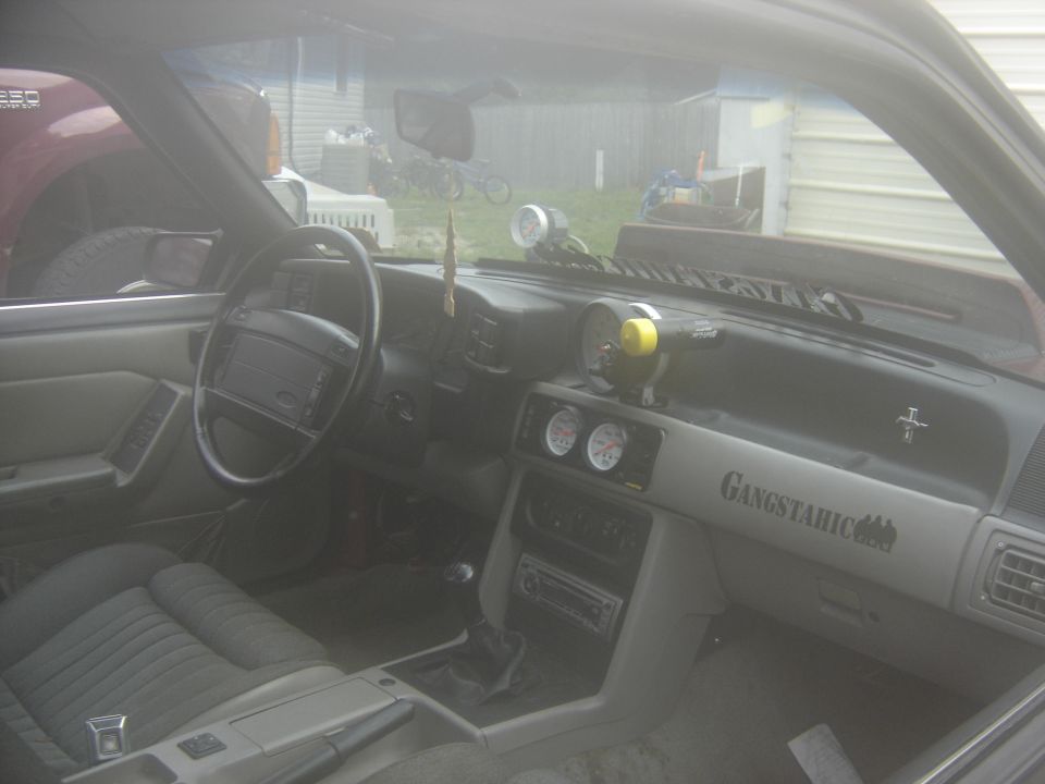 Interior of a 1988 Ford Mustang with aftermarket gauges and 'Gangstahic' decal on the dash