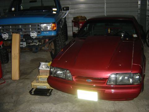 1988 Ford Bronco - A red car with a custom hood scoop is parked next to a blue off-road vehicle.