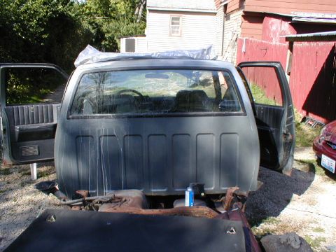 1998 Ford Taurus - pickup project with the cab pulled and doors open, viewed from the rear over a bare frame, in a backyard near a barn.