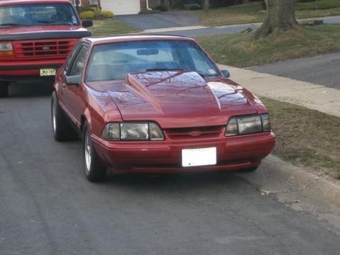1988 Ford Bronco - Red coupe with aftermarket hood scoop parked on street next to a red Ford pickup truck.