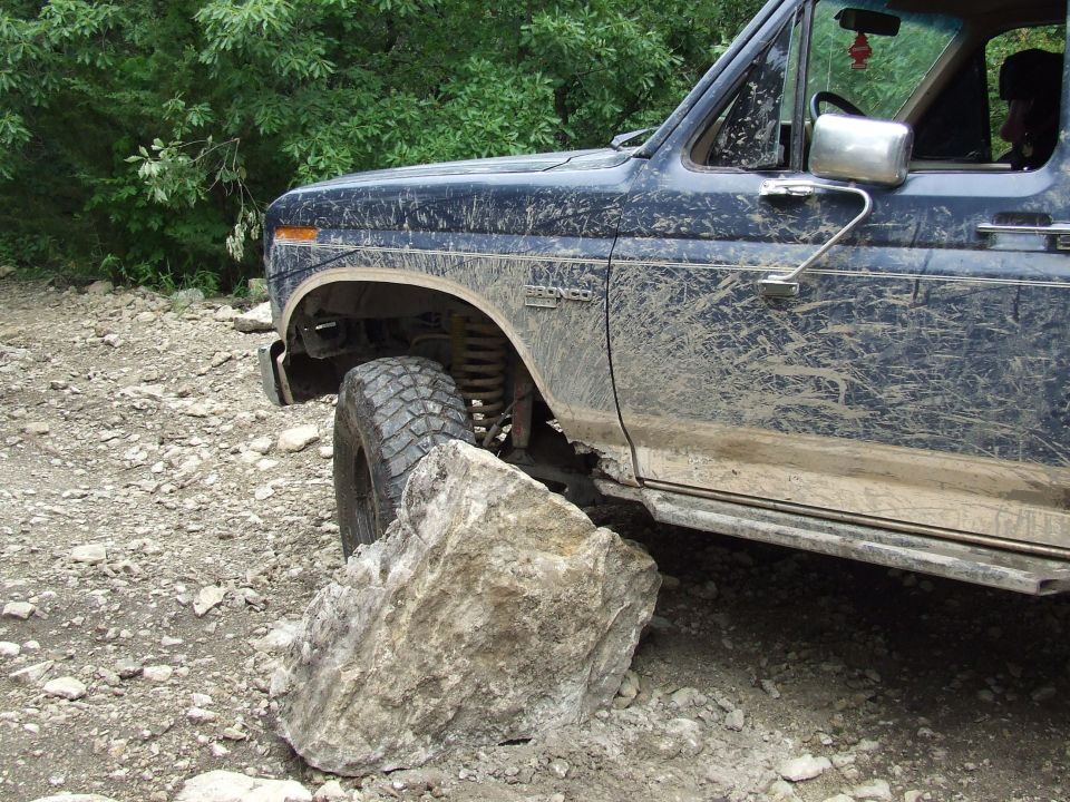 Mud-splattered dark blue Ford Bronco with a large rock in front of its front tire