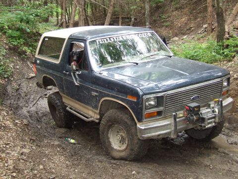 1986 Ford Bronco - This 1986 Ford Bronco navigates a muddy trail with a dog in the driver's seat and a winch mounted on the front.