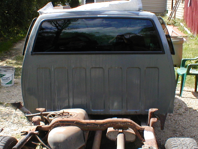 Rear of a gray pickup truck cab with a large window and ribbed bed paneling
