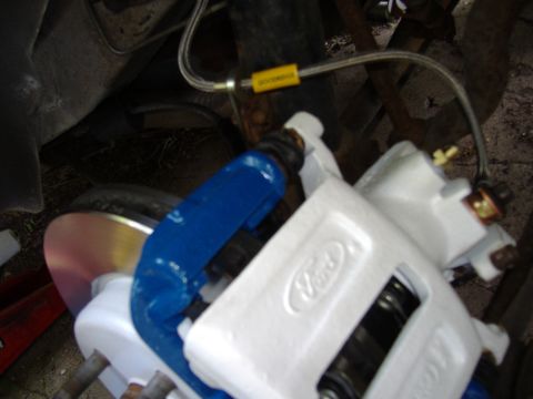 1998 Ford Taurus - A close-up view of a Ford brake caliper assembly, showing the white caliper body and blue bracket.