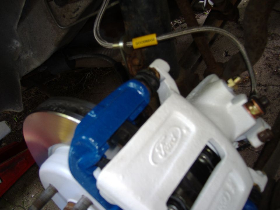 Close-up of a white Ford brake caliper with a blue bracket and brake rotor