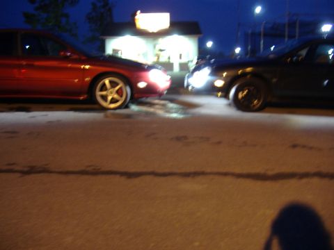 1998 Ford Taurus - Two cars parked head-to-head at night in front of a brightly lit building.