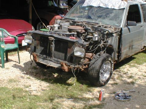 1998 Ford Taurus - Damaged pickup truck front end with engine exposed, red car and chair in background.
