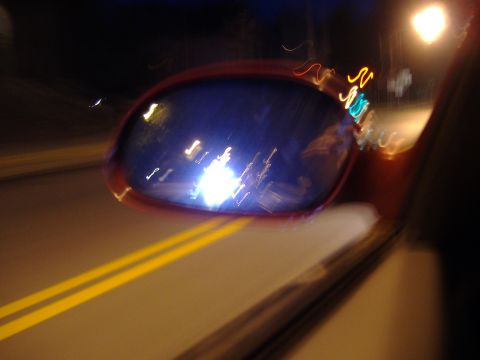 1998 Ford Taurus - A blurry night shot captures the reflection in a car's side mirror, with double yellow lines visible on the road.
