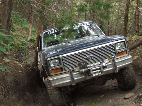 1986 Ford Bronco - Ford Bronco tackles a muddy, wooded trail with a winch mounted on the front bumper.