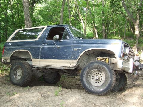 1986 Ford Bronco - A lifted blue and tan Ford Bronco sits off-road with large tires and a modified suspension.