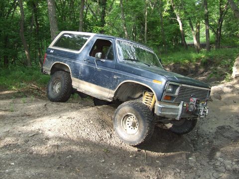 1986 Ford Bronco - Ford Bronco navigates a steep, muddy incline in a wooded area.