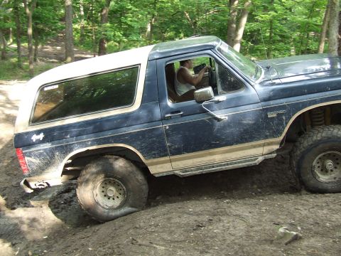 1986 Ford Bronco - Ford Bronco navigating a muddy off-road course with a driver at the wheel.