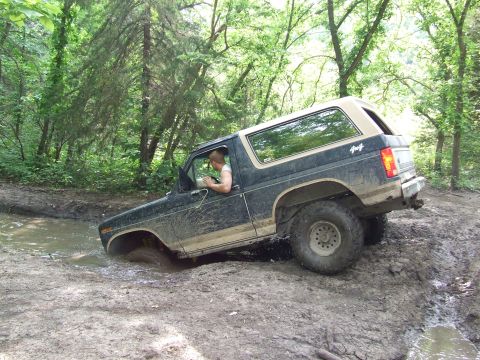 1986 Ford Bronco - A Ford Bronco navigates a muddy trail in a wooded area.