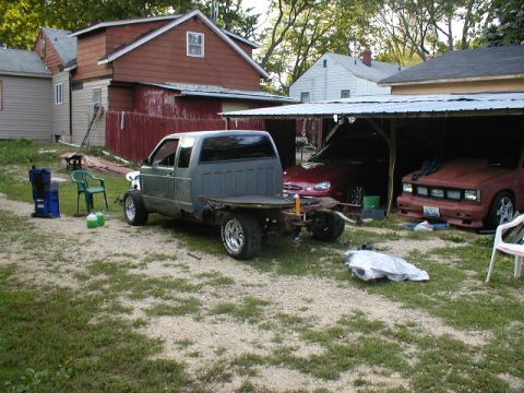 1998 Ford Taurus - A gray flatbed truck sits in a yard with other vehicles nearby.