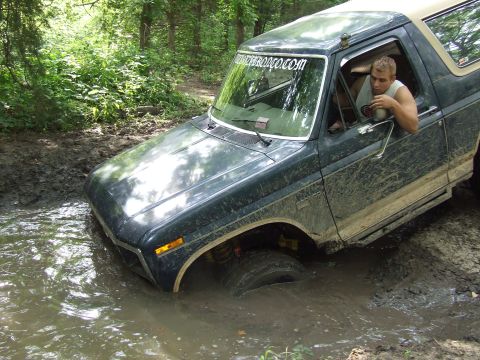 1986 Ford Bronco - A dark green 1986 Ford Bronco navigates a muddy trail, getting stuck in the water.