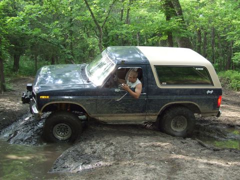 1986 Ford Bronco - Ford Bronco navigating a muddy off-road path with trees surrounding it.