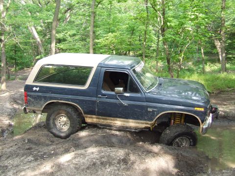 1986 Ford Bronco - This Ford Bronco is navigating a muddy trail with one wheel deep in a water hazard.