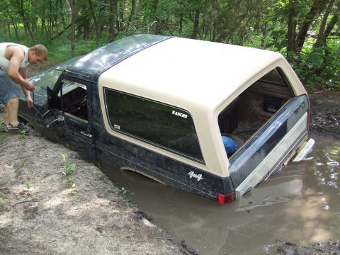 1986 Ford Bronco - A man attempts to free a Ford Bronco that is stuck in a muddy ditch.