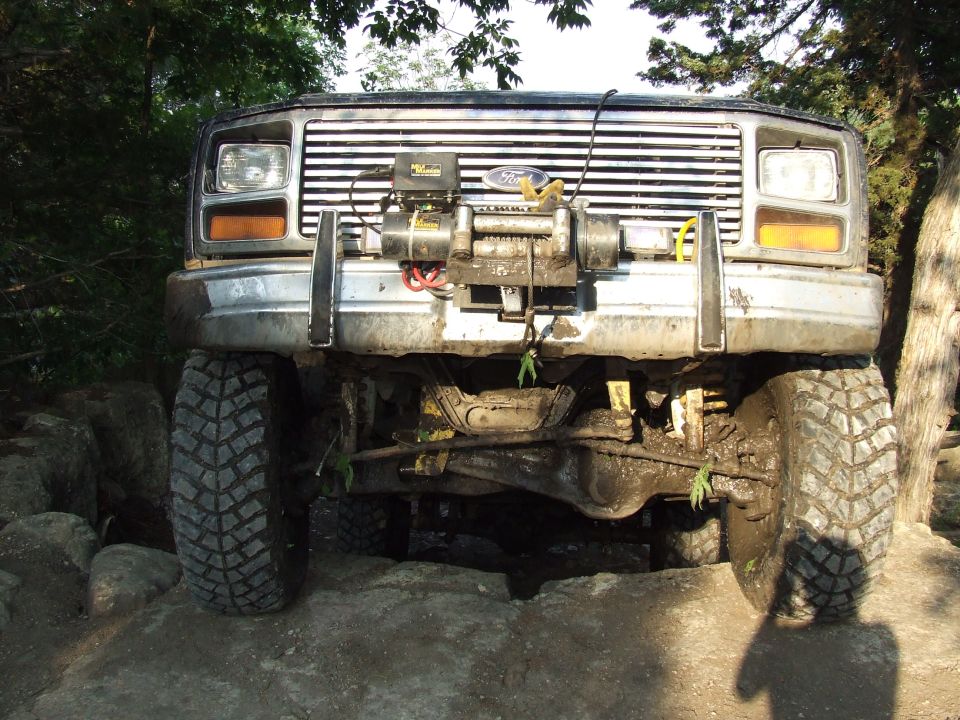 Front view of a muddy 1980s Ford Bronco with a winch mounted on the bumper