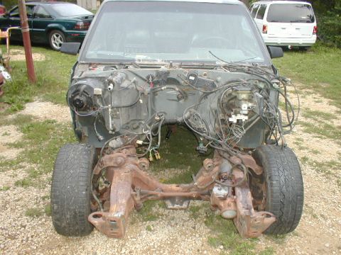 1998 Ford Taurus - Vehicle chassis with engine bay exposed, parked outdoors with other vehicles visible.