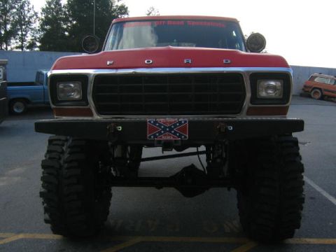 1979 Ford Bronco - A red 1979 Ford Bronco is parked, showing its front grille and massive tires.