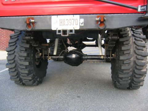 1979 Ford Bronco - The rear of a heavily modified vehicle is shown, oversized tires and a custom bumper with tow hooks.