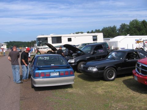 1989 Ford Mustang - A blue Ford Mustang is parked on grass next to other vehicles, with an RV and trailers in the background.