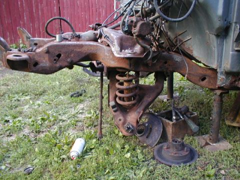 1998 Ford Taurus - Disassembled and heavily corroded vehicle chassis components lie scattered on the grass.