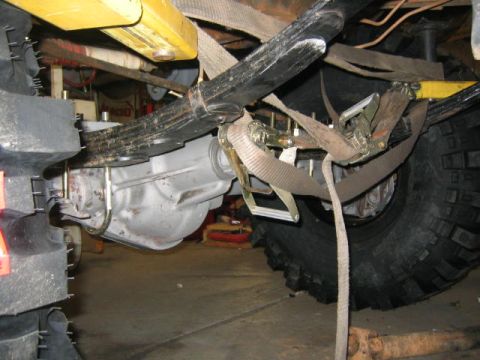 1979 Ford Bronco - The underside of a vehicle is shown, focusing on the suspension components and a large tire, secured with tie-down straps.