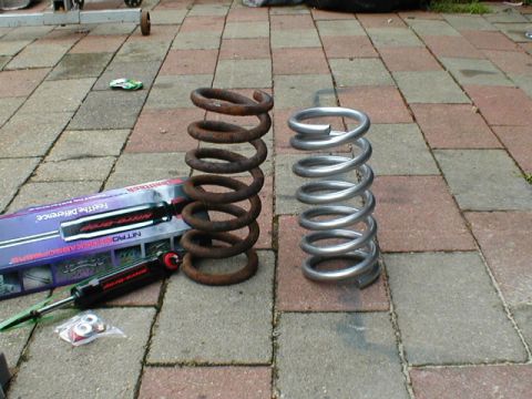 1998 Ford Taurus - A comparison of old and new coil springs, alongside a shock absorber package, displayed on a paved surface.