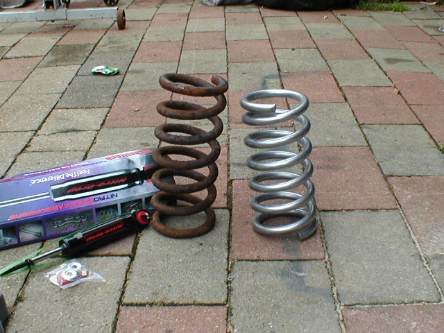 Two coil springs, one rusty and one new, next to a shock absorber box