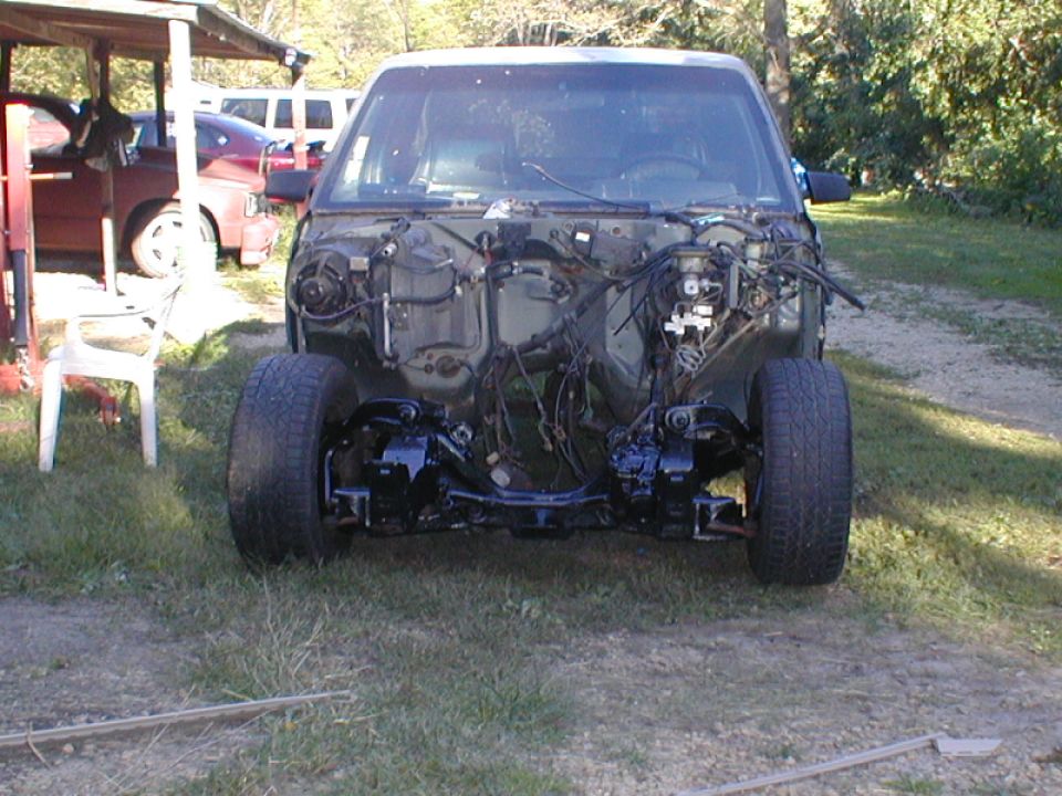 Front view of a car chassis with engine bay stripped bare, showing suspension and wiring
