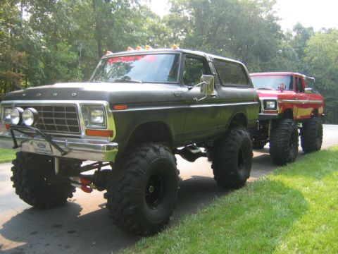 1979 Ford Bronco - A dark green/olive 1970s Ford Bronco full-size SUV with a massive lift kit, oversized off-road mud tires, chrome grille and tube front bump…