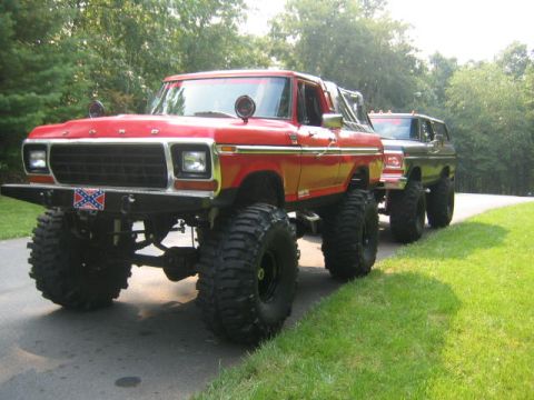 1979 Ford Bronco - A lifted red Ford Bronco with a white top sits on large off-road mud tires and black wheels, parked on a paved driveway with a Confederate…