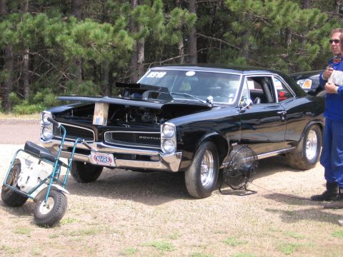 1989 Ford Mustang - A black Pontiac muscle car is parked with its hood open, a mini bike in front and a fan nearby.